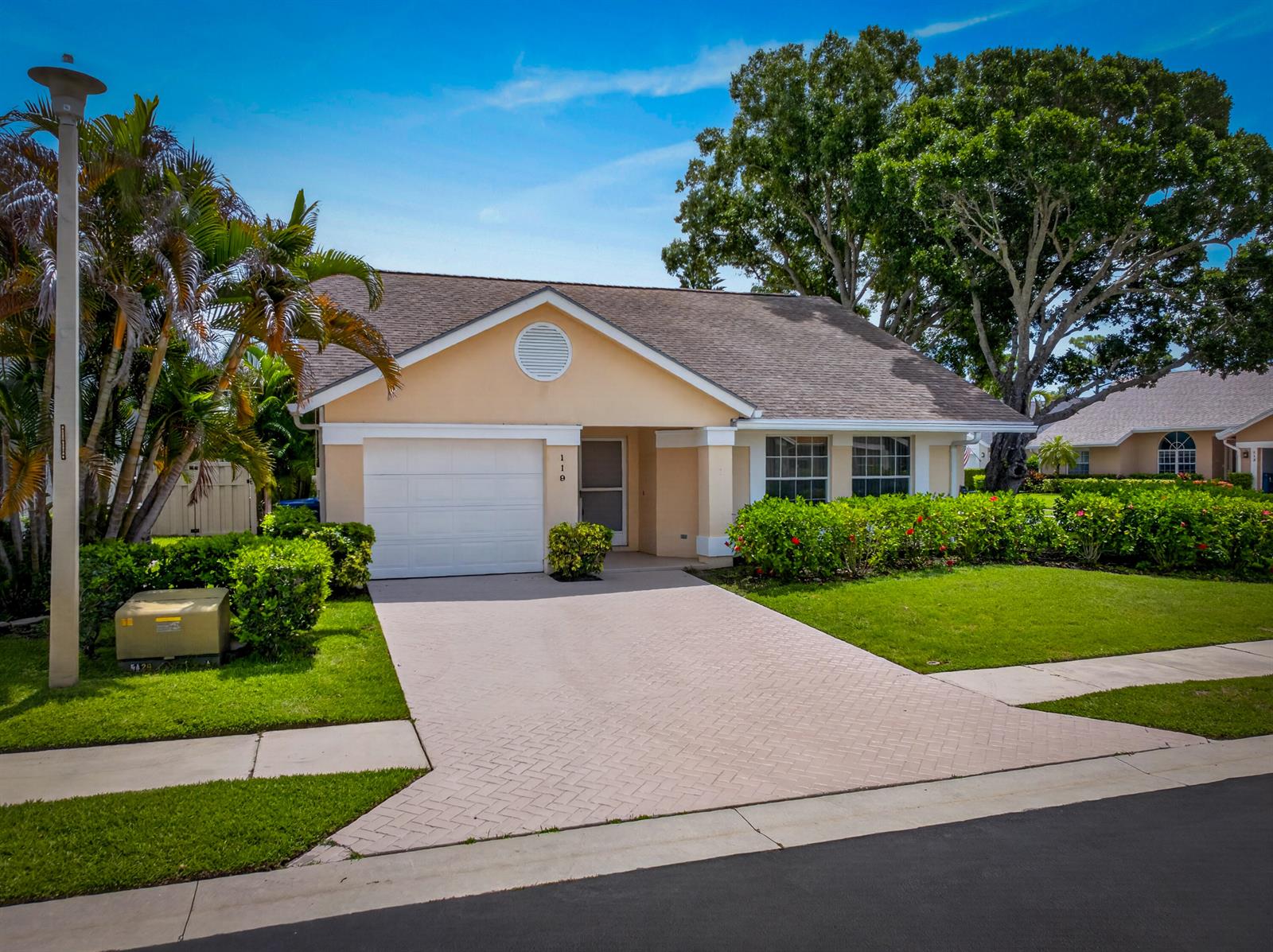A single-story house with a beige exterior, a paved driveway, and a front-facing garage — 119 Adobe Circle, Jupiter FL 33458, JUPITER, FL