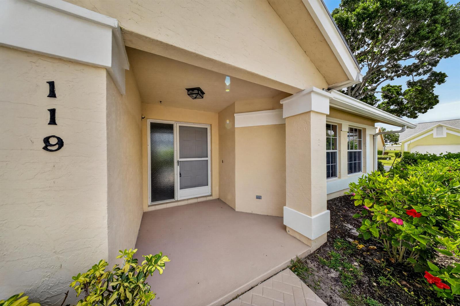 A beige house exterior features a covered entryway with a screen door and house numbers — 119 Adobe Circle, Jupiter FL 33458, JUPITER, FL