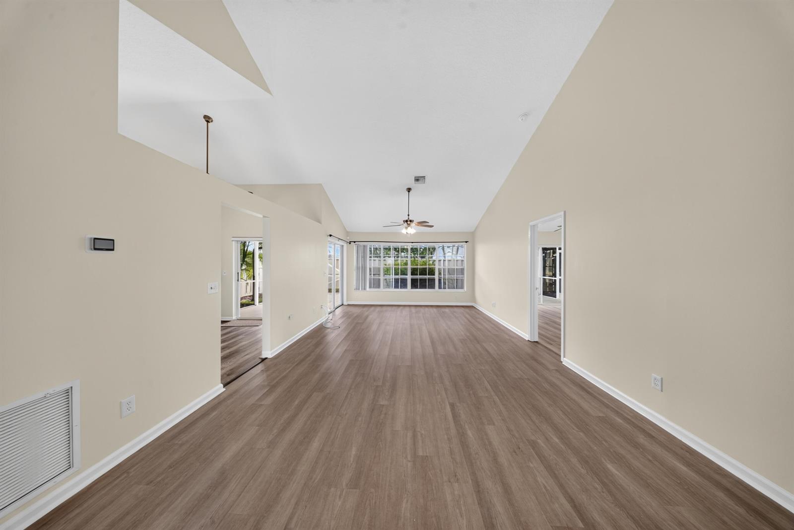 An empty living room with vaulted ceilings, wood-look flooring, and a ceiling fan — 119 Adobe Circle, Jupiter FL 33458, JUPITER, FL