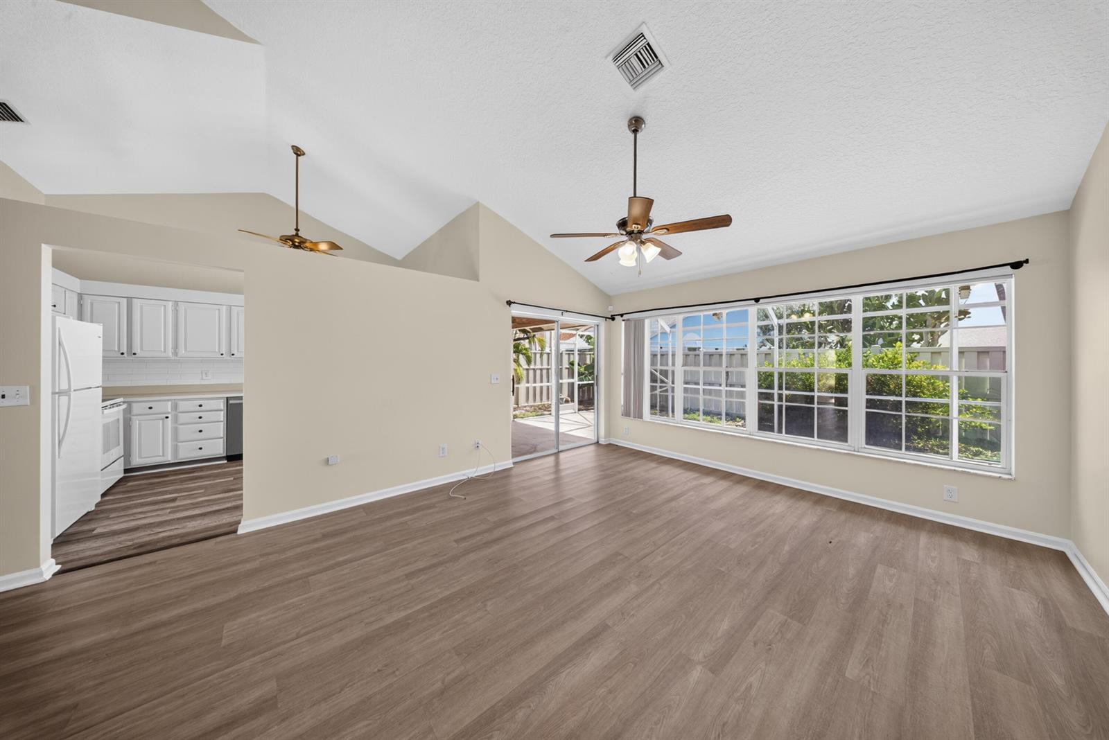 An empty living room with vaulted ceilings, wood-look flooring, and a view of the patio — 119 Adobe Circle, Jupiter FL 33458, JUPITER, FL