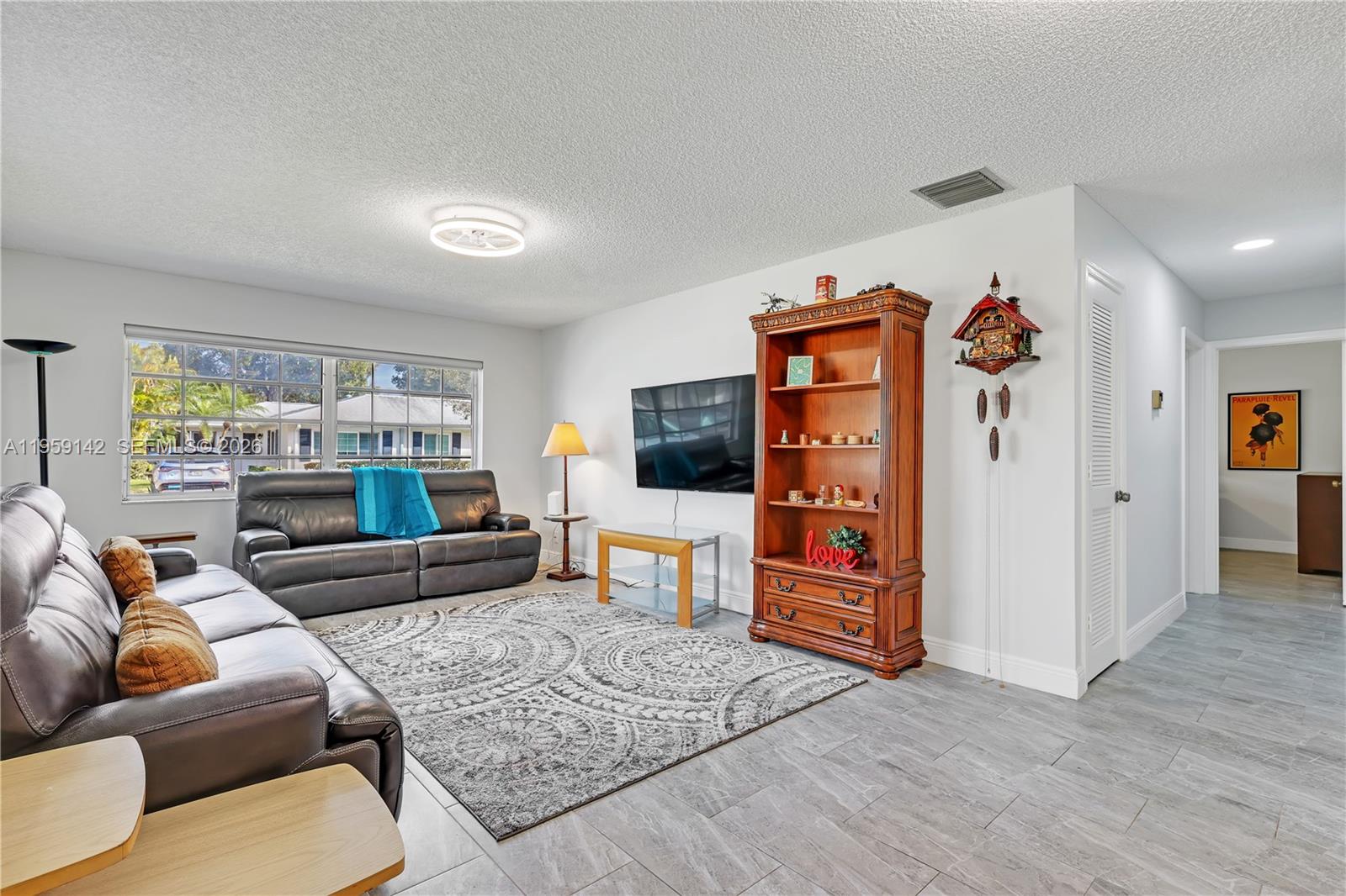 A living room features gray tile flooring, a leather sofa, a television, and a wooden bookcase — 10115 44th Way S # 409, Boynton Beach FL 33436, BOYNTON BEACH, FL