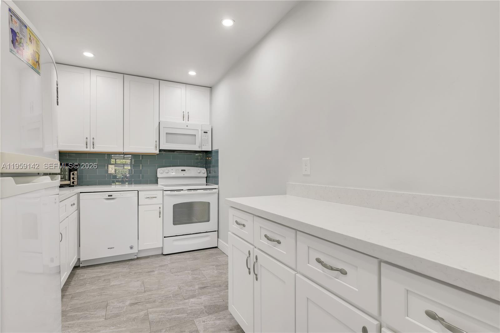A kitchen features white cabinets, white appliances, a blue tile backsplash, and light countertops — 10115 44th Way S # 409, Boynton Beach FL 33436, BOYNTON BEACH, FL