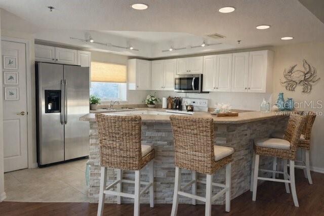 A kitchen features white cabinets, stainless steel appliances, and a stone-faced island with wicker stools — 5300 S ATLANTIC AVENUE UNIT 8-401, NEW SMYRNA BEACH, FL