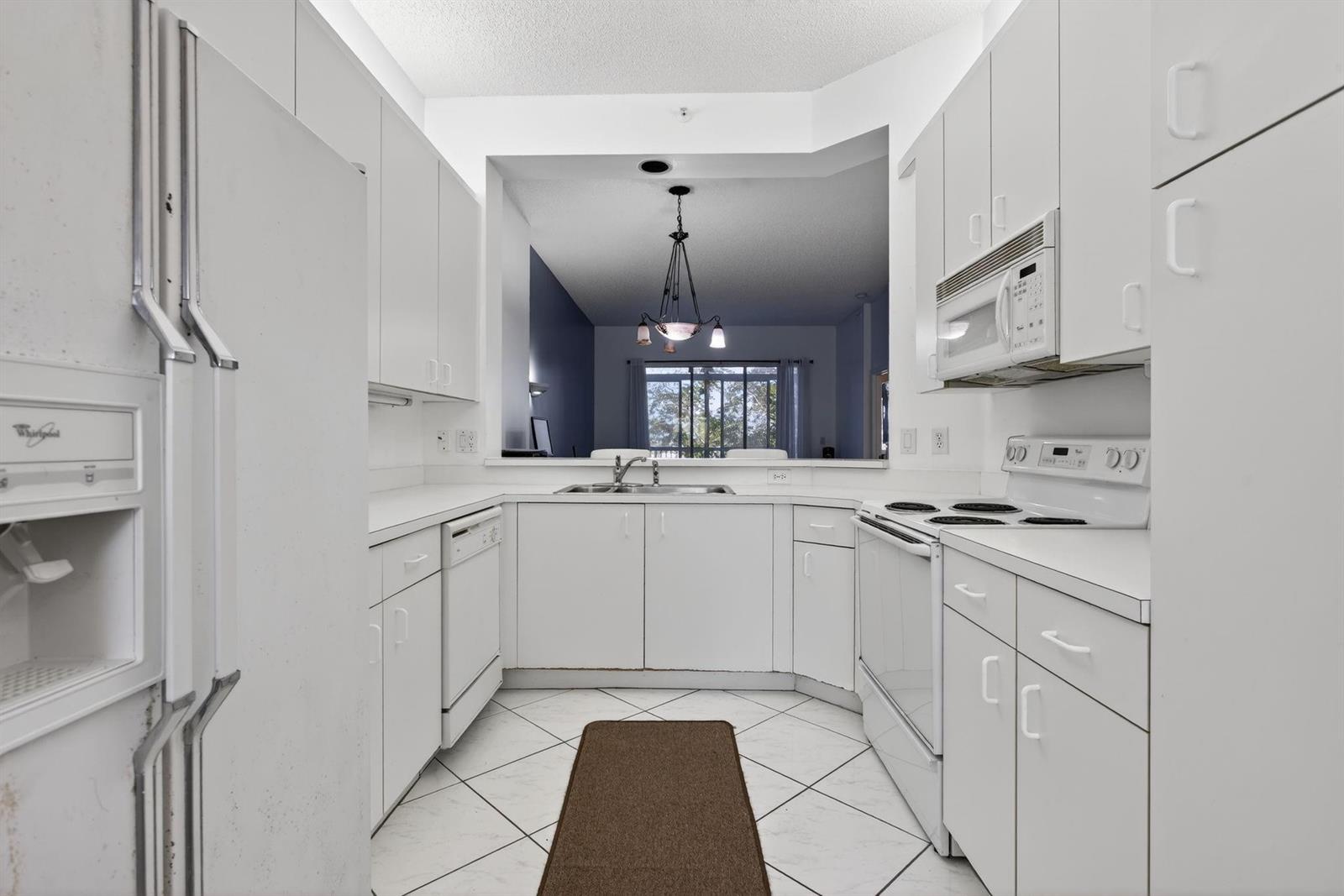 A white galley kitchen features white cabinets, appliances, and tile flooring with a pass-through window — 9575 Weldon Circle Apt C413, Tamarac FL 33321, TAMARAC, FL