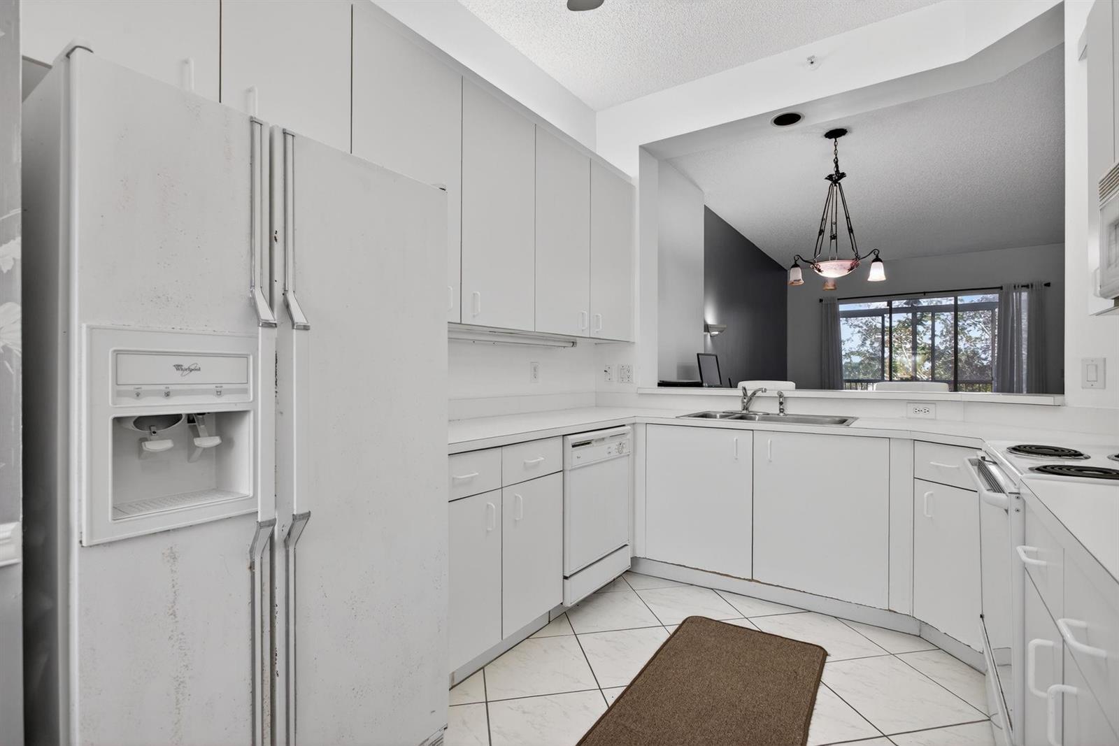 A white kitchen features white cabinetry, white appliances, and a pass-through window to the living area — 9575 Weldon Circle Apt C413, Tamarac FL 33321, TAMARAC, FL