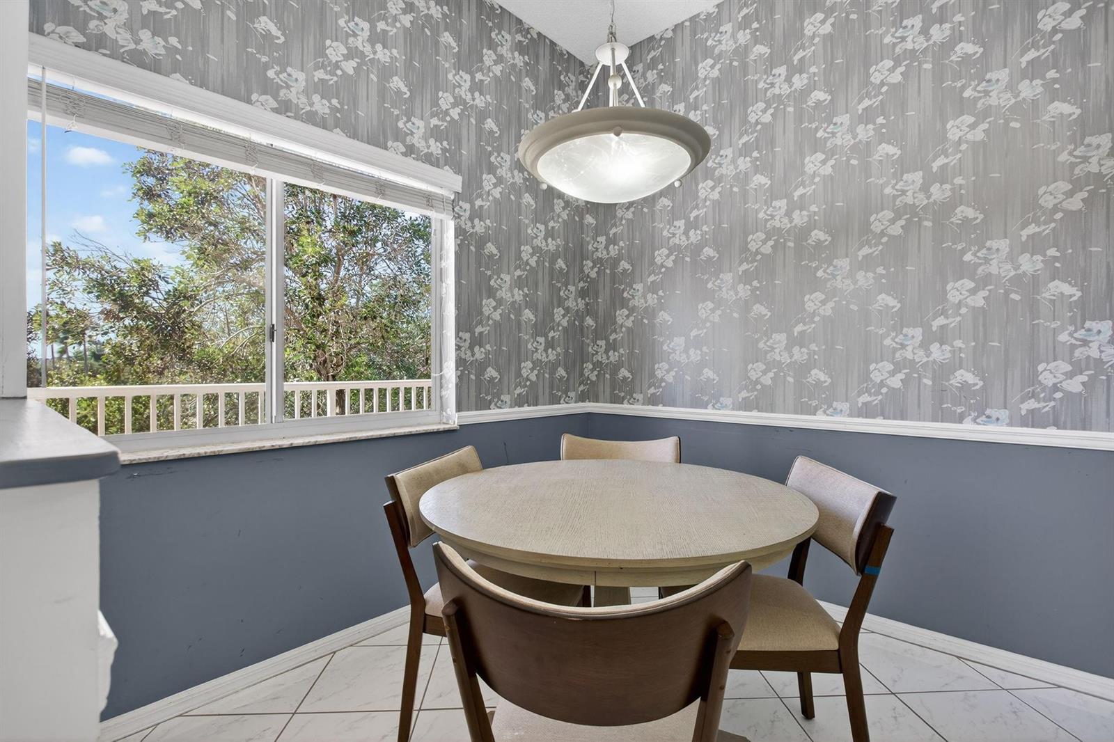 A dining area features a round table, four chairs, floral wallpaper, and a large window — 9575 Weldon Circle Apt C413, Tamarac FL 33321, TAMARAC, FL