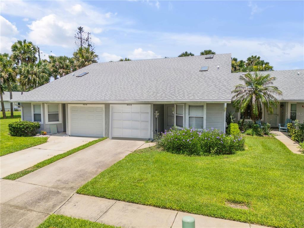 A single-story duplex with gray siding, two white garage doors, and a landscaped front yard — 937 MEADOW VIEW DRIVE UNIT B, PORT ORANGE, FL