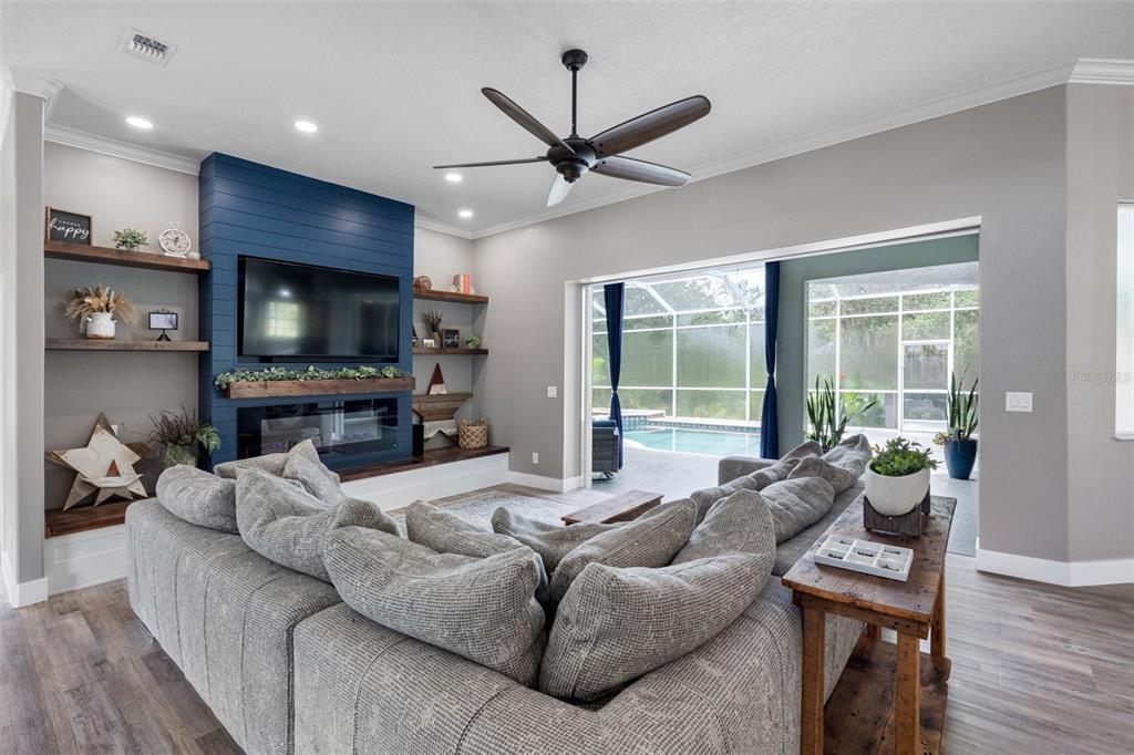 A living room features a blue shiplap fireplace, open shelving, and a view of a pool — 1079 RIVERSIDE RIDGE ROAD, TARPON SPRINGS, FL
