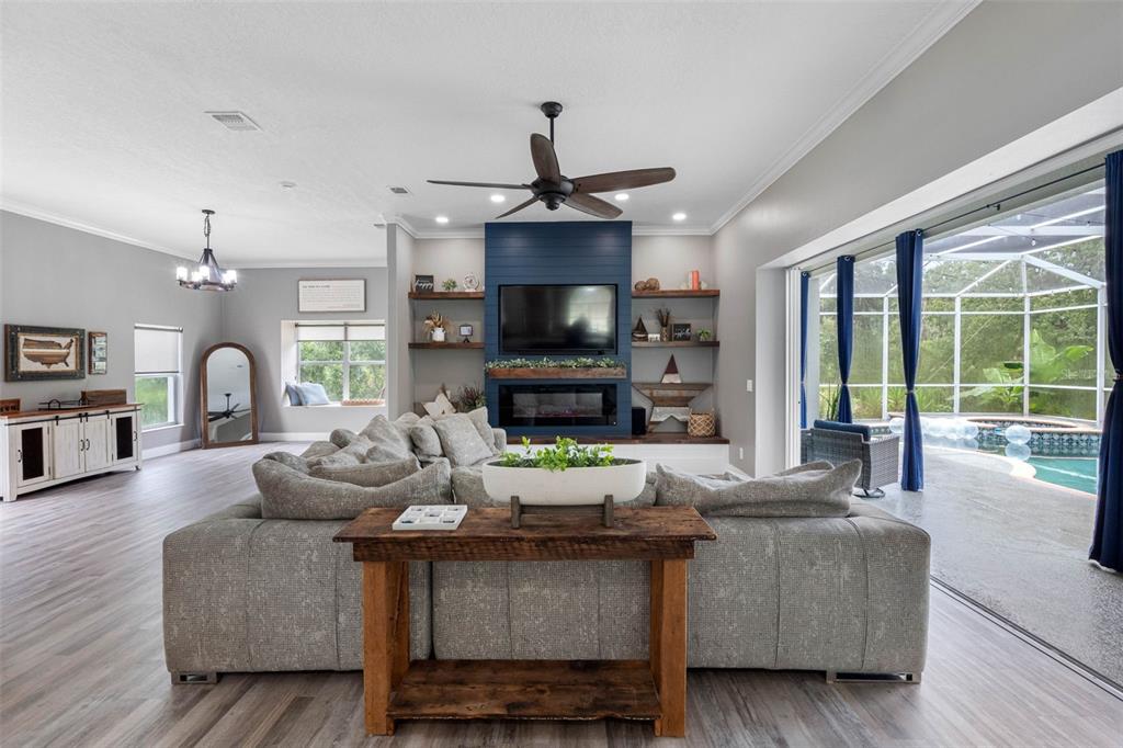 A living room features a blue fireplace accent wall, a large sectional, and sliding glass doors — 1079 RIVERSIDE RIDGE ROAD, TARPON SPRINGS, FL