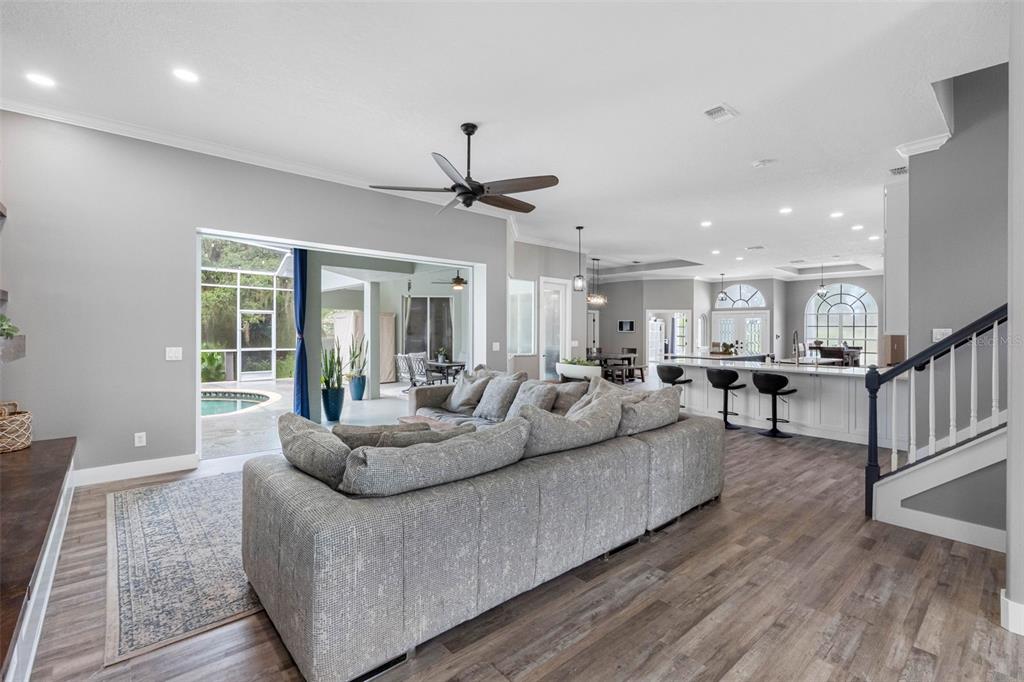 A living room with a large sectional sofa, wood-look flooring, and an open kitchen area — 1079 RIVERSIDE RIDGE ROAD, TARPON SPRINGS, FL