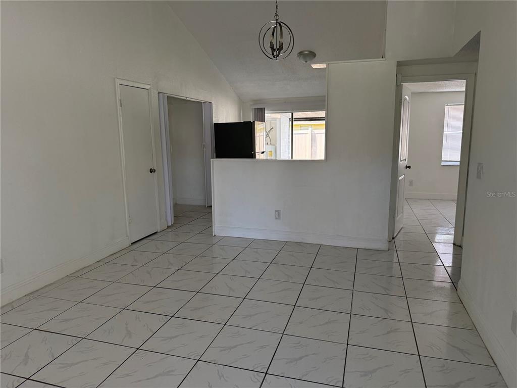 A room with white tiled floors, a vaulted ceiling, and a partial wall kitchen pass-through — 10205 BELLHURST COURT, TAMPA, FL