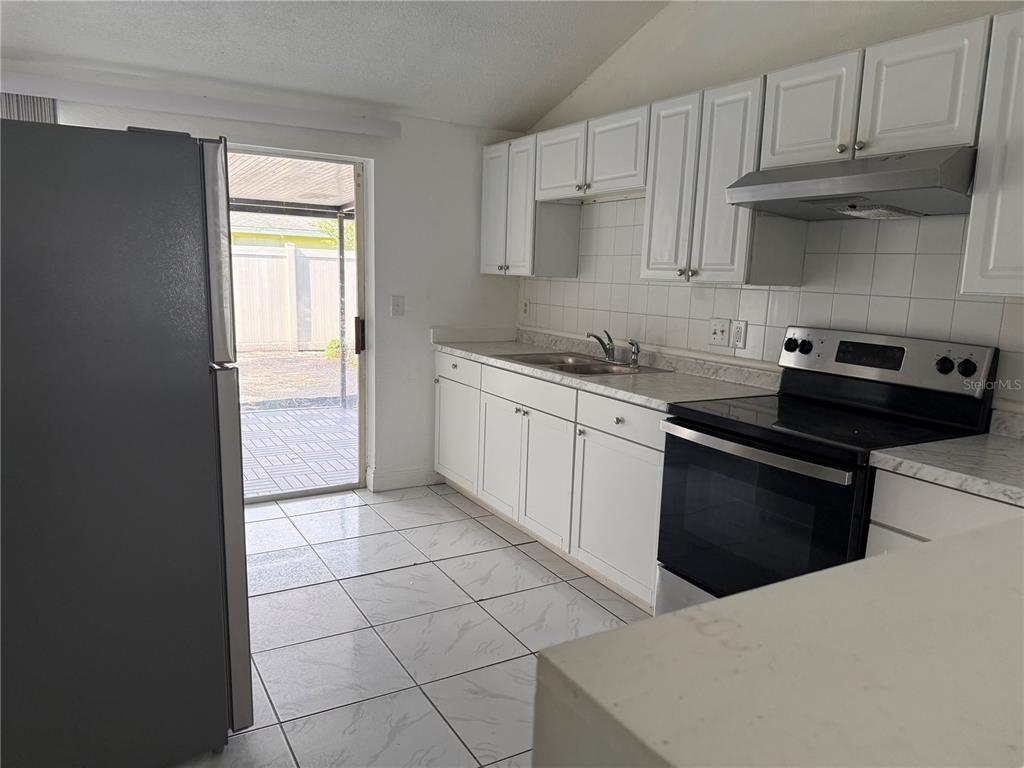 A kitchen with white cabinets, a stainless steel refrigerator, and a sliding glass door — 10205 BELLHURST COURT, TAMPA, FL