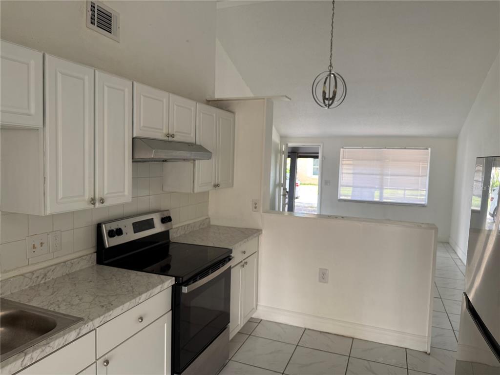 A kitchen with white cabinets, stainless steel appliances, and tile flooring opens to a living area — 10205 BELLHURST COURT, TAMPA, FL