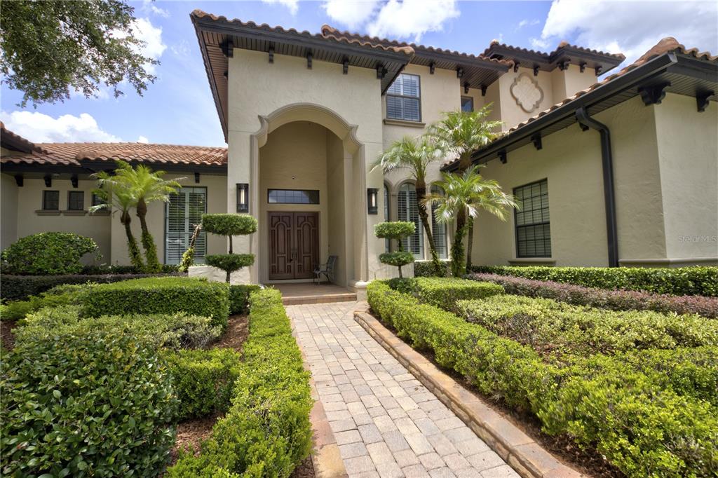 A paved walkway leads to the arched entryway of a stucco house with tile roofing — 3318 SUNSET VIEW COURT, LONGWOOD, FL