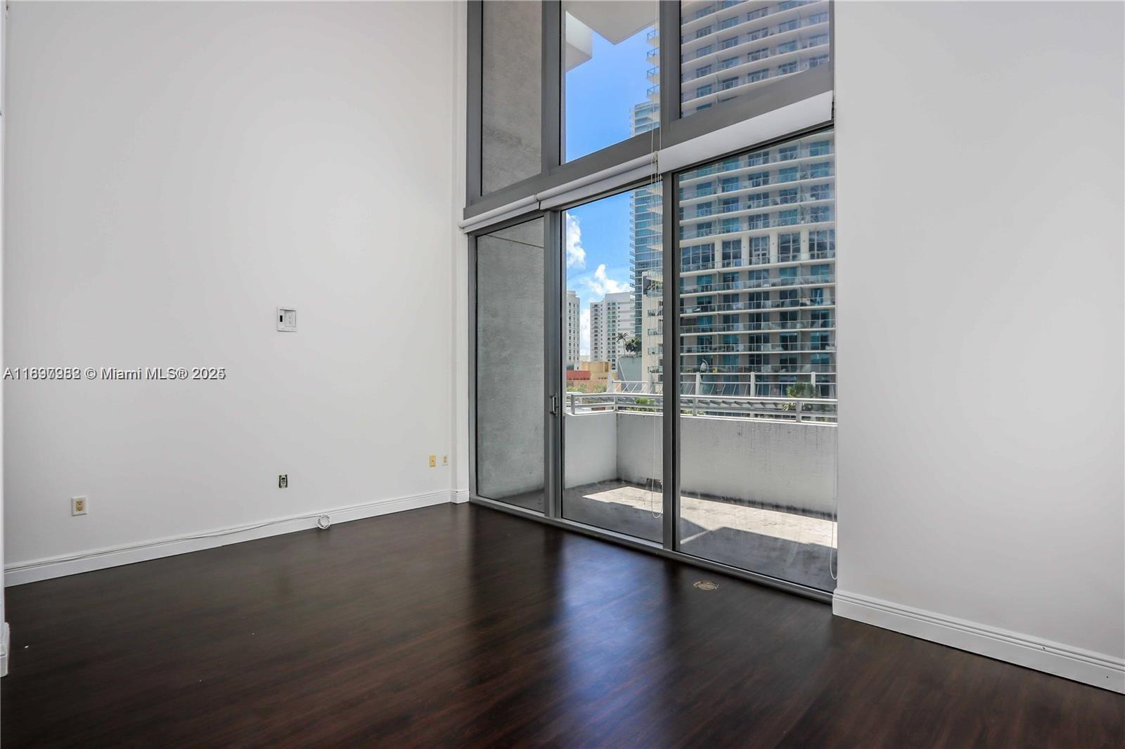 An empty room features dark wood flooring, white walls, and floor-to-ceiling windows with balcony access — 1050 Brickell Ave # 414, Miami FL 33131, MIAMI, FL