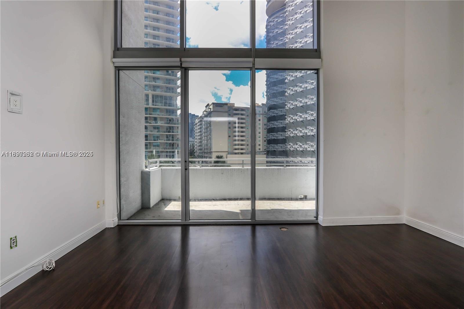 An empty room with dark wood floors and floor-to-ceiling windows overlooking a balcony and city — 1050 Brickell Ave # 414, Miami FL 33131, MIAMI, FL