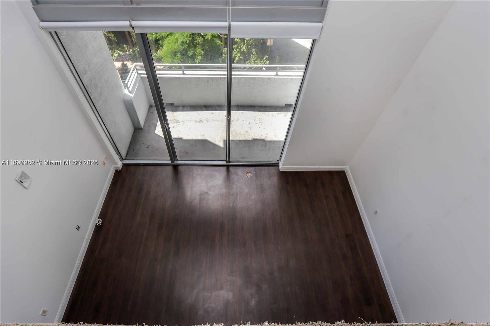 An empty room with dark wood-look flooring features a large sliding glass door to a balcony — 1050 Brickell Ave # 414, Miami FL 33131, MIAMI, FL