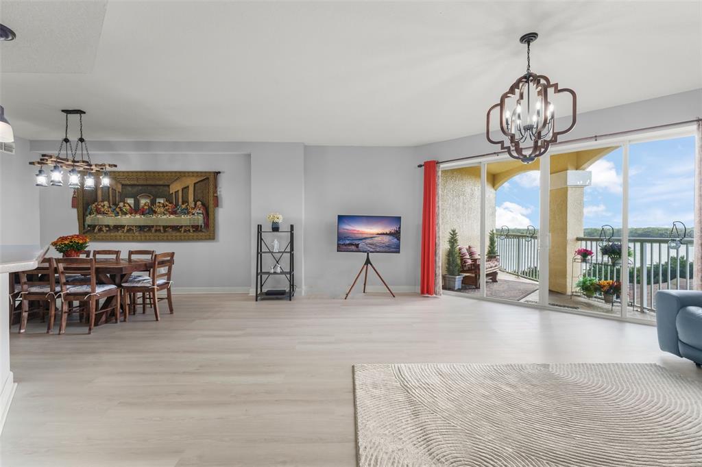 An open-concept living and dining area features light wood flooring, a balcony, and chandeliers — 6336 BUFORD STREET UNIT 809, ORLANDO, FL