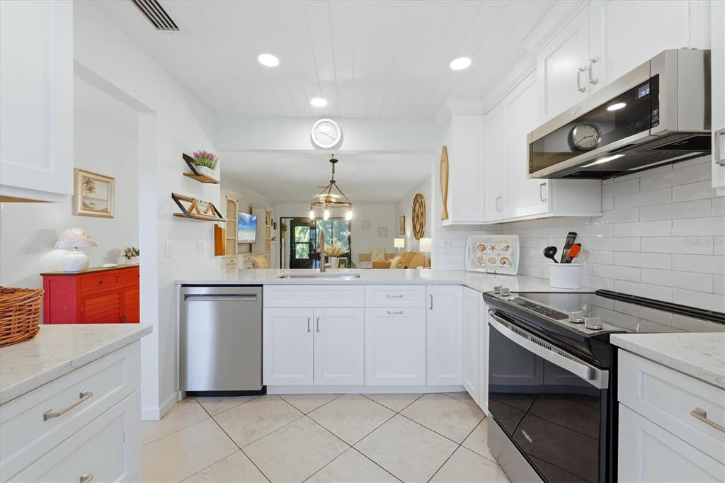 A white kitchen features stainless steel appliances, tile flooring, and an open view to living — 106 JOSE GASPAR DRIVE UNIT 106, ENGLEWOOD, FL