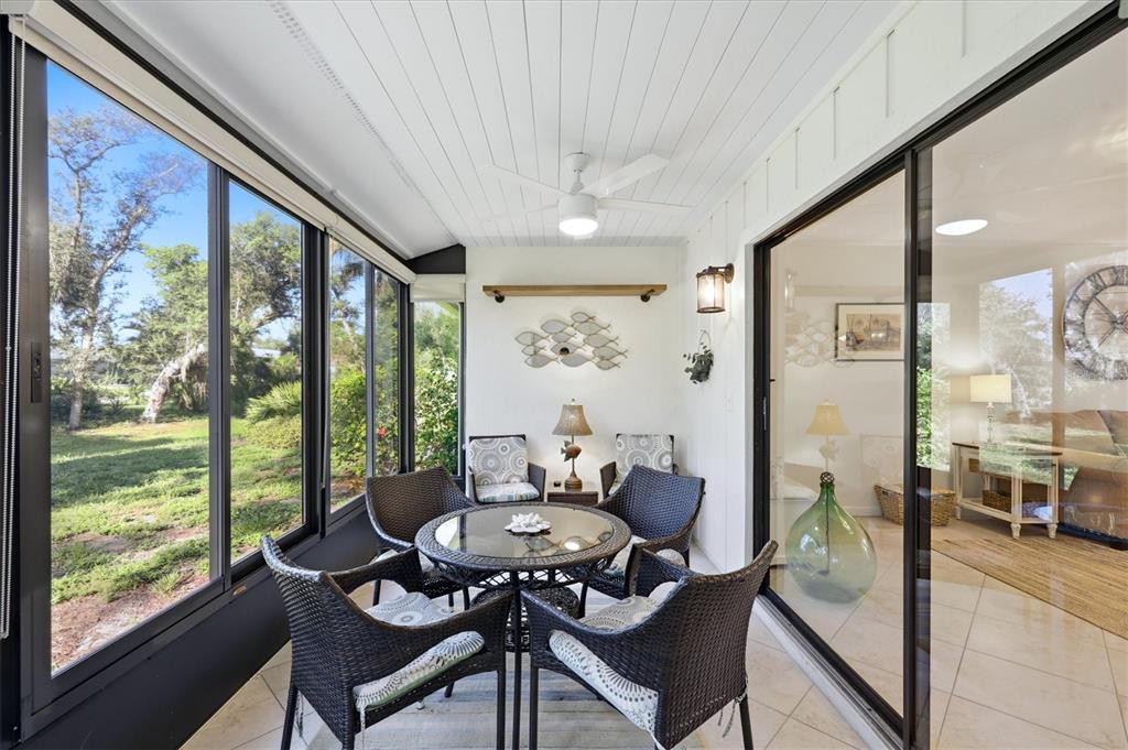 A sunroom features a glass-topped wicker table, four chairs, a ceiling fan, and large windows — 106 JOSE GASPAR DRIVE UNIT 106, ENGLEWOOD, FL