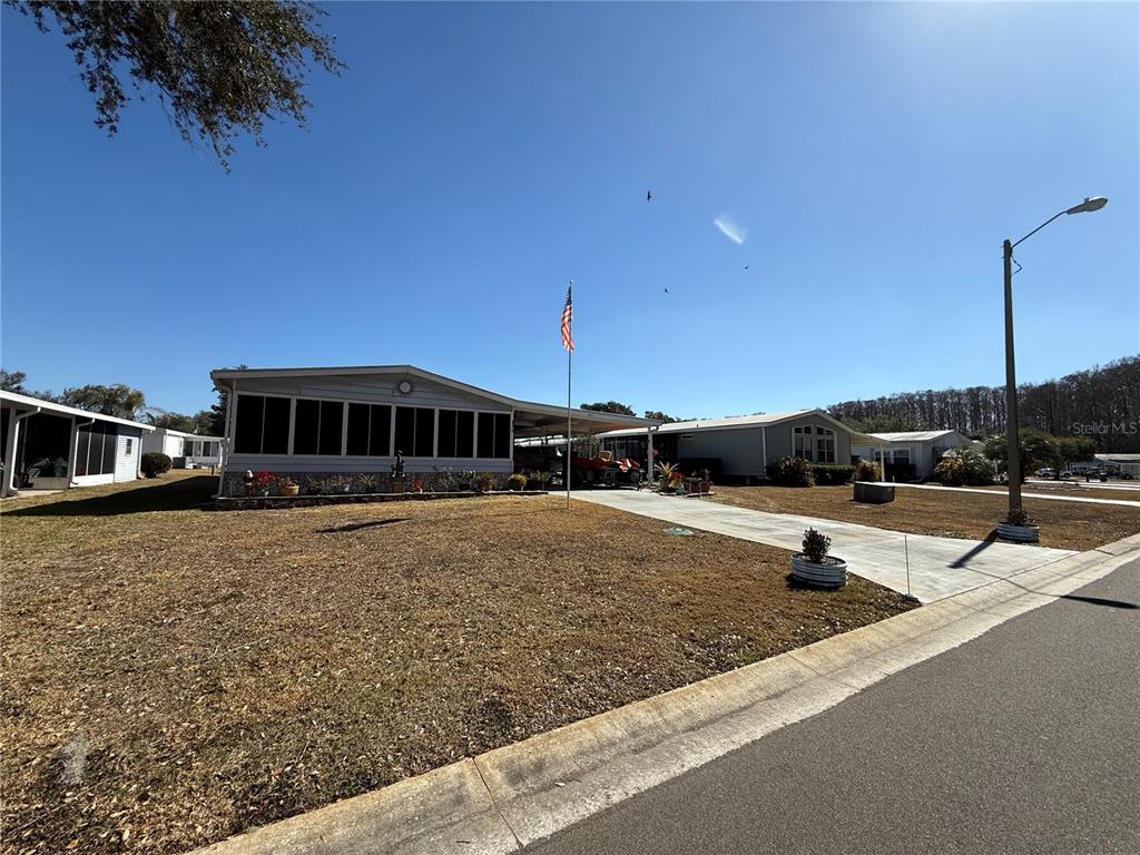 A single-story manufactured home with a screened porch, carport, and American flag in the yard — 805 OAK BOULEVARD, WILDWOOD, FL