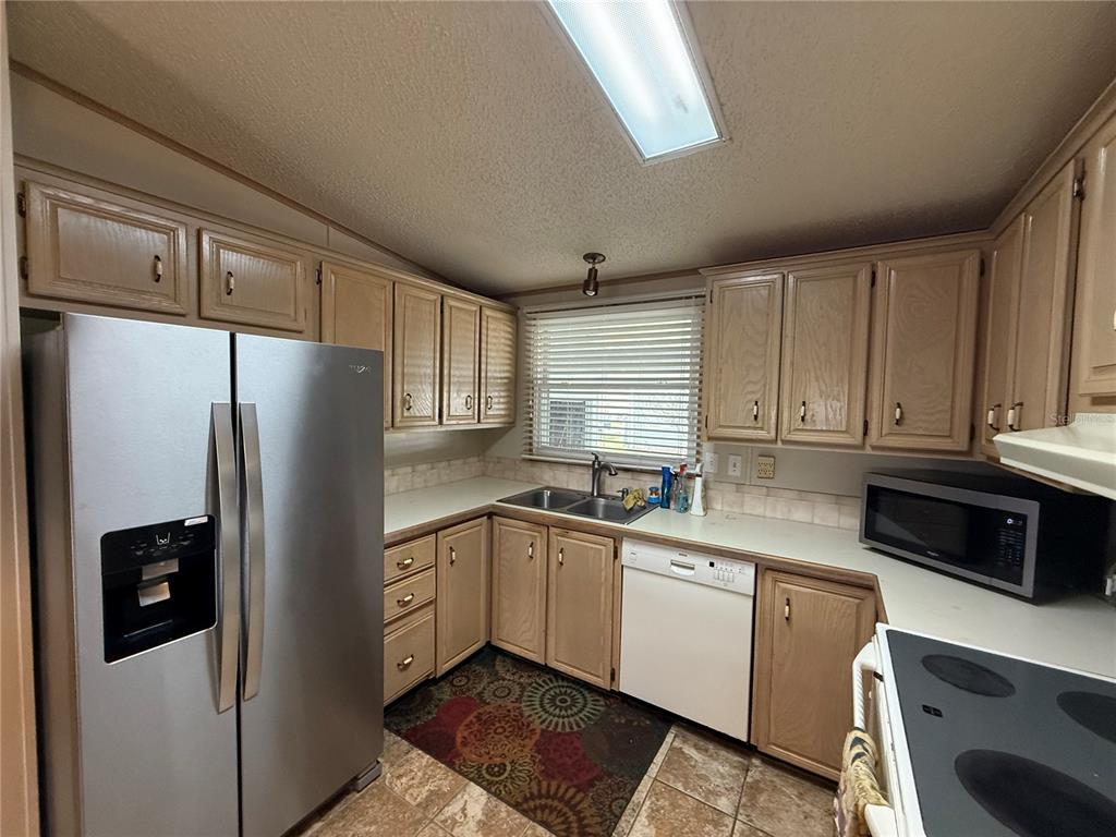 A kitchen features light wood cabinets, stainless steel appliances, a double sink, and tile flooring — 805 OAK BOULEVARD, WILDWOOD, FL