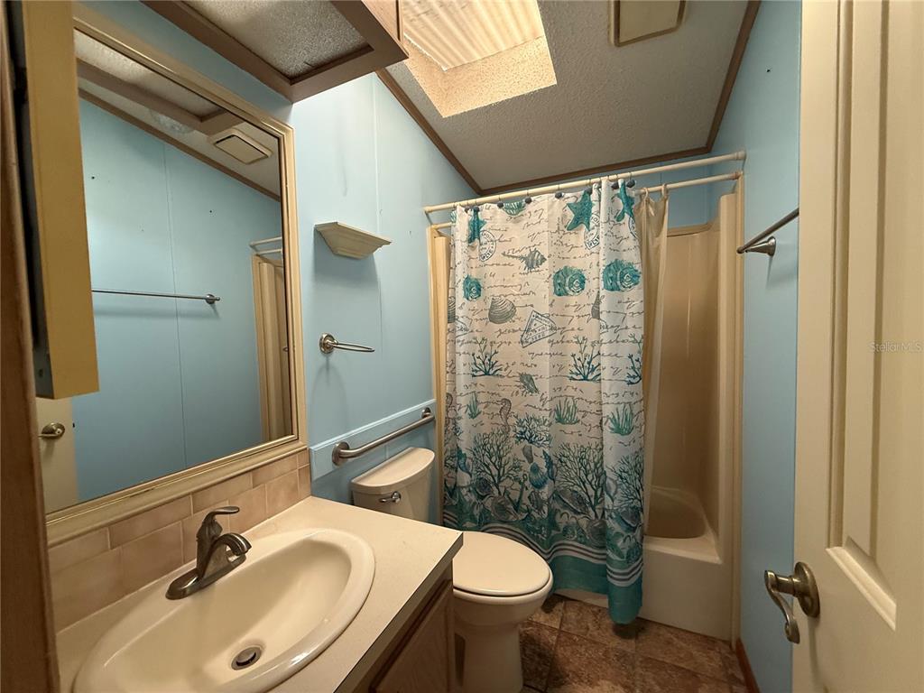 A bathroom features a vanity, a toilet, and a shower-tub combination with a coastal-themed curtain — 805 OAK BOULEVARD, WILDWOOD, FL