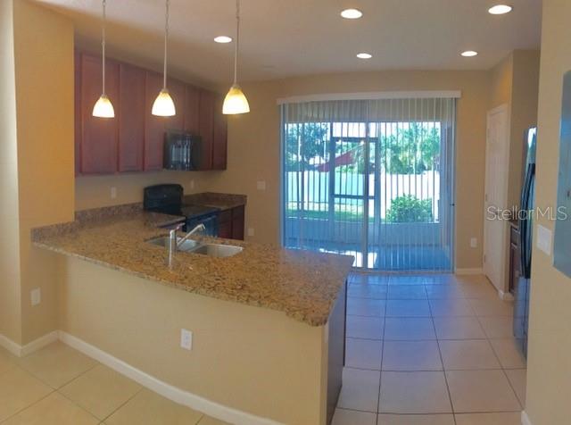 A kitchen with granite countertops, wooden cabinets, and a sliding glass door to a patio — 1102 CHELSEA DRIVE, DAVENPORT, FL