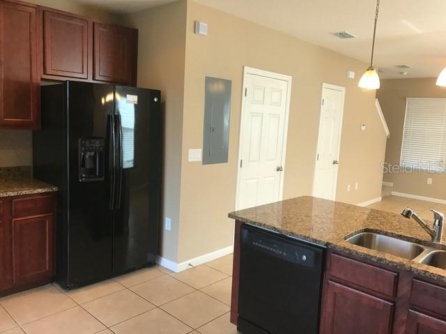A kitchen features dark wood cabinets, a black refrigerator, granite countertops, and tile flooring — 1102 CHELSEA DRIVE, DAVENPORT, FL