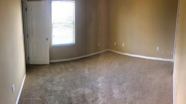 An empty bedroom features beige carpet, tan walls, and a window with white blinds — 1102 CHELSEA DRIVE, DAVENPORT, FL