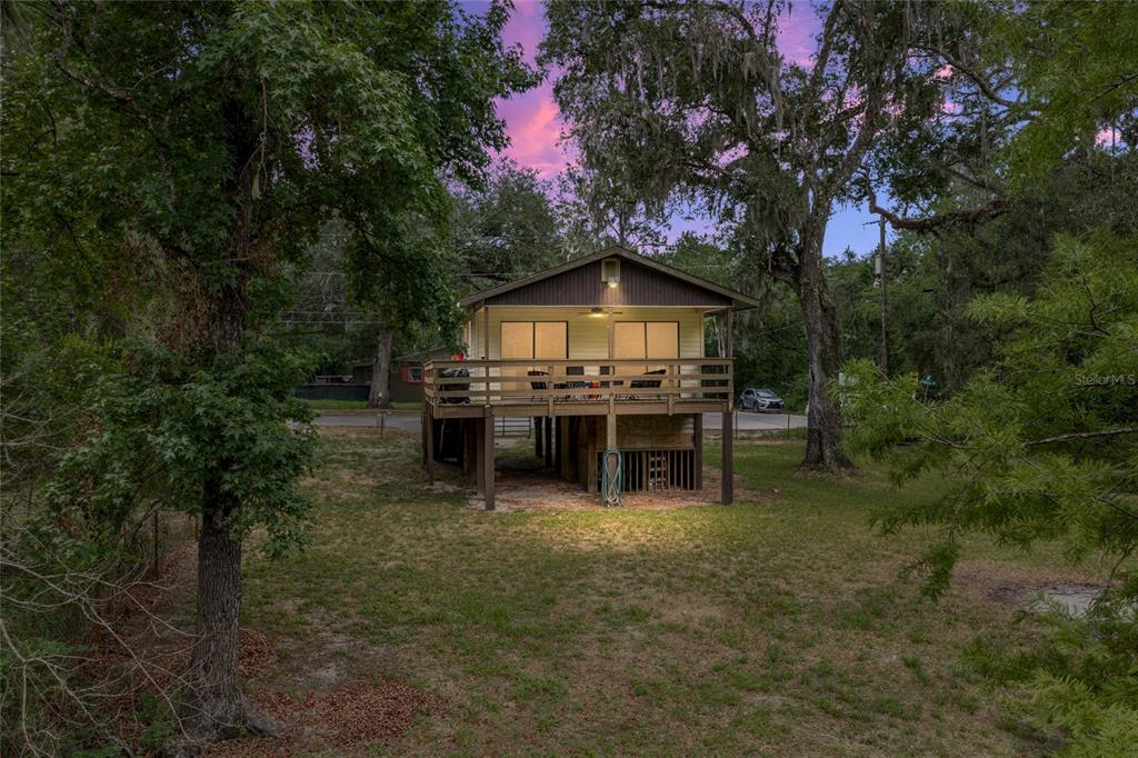 An elevated house with a wooden deck stands in a grassy, tree-filled yard — 33065 CEDONIA ROAD, DADE CITY, FL
