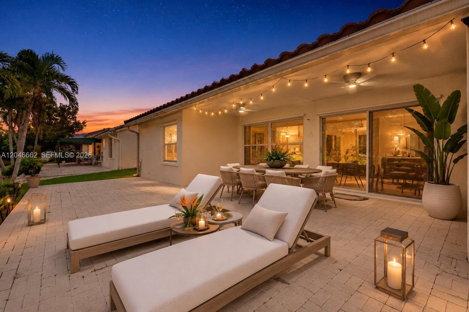 A paved patio features two lounge chairs, a dining set, and string lights at dusk — 3450 Dunes Vista Dr, Pompano Beach FL 33069, POMPANO BEACH, FL