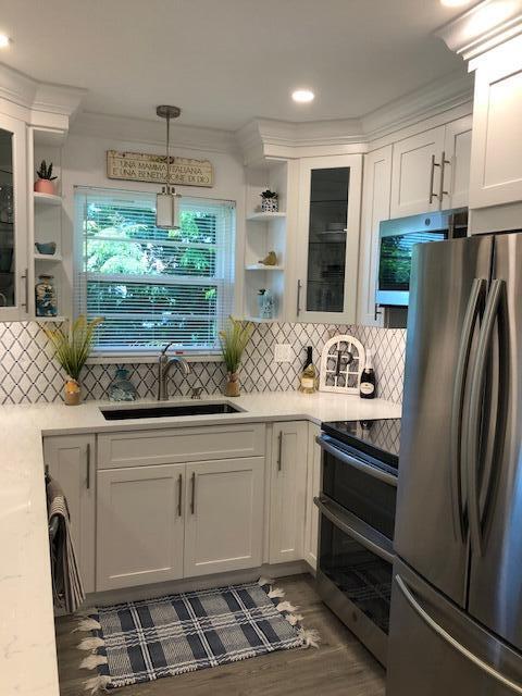 A bright kitchen features white cabinets, stainless steel appliances, a farmhouse sink, and patterned backsplash — 2600 SE Ocean Boulevard # Q8, Stuart FL 34996, STUART, FL