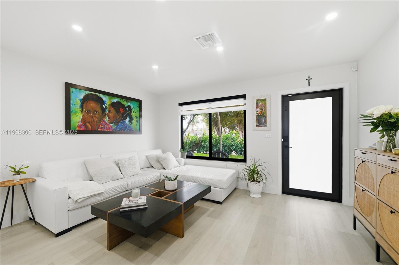 A bright living room features a white sectional sofa, a black coffee table, and a door — 7491 Raleigh St, Hollywood FL 33024, HOLLYWOOD, FL