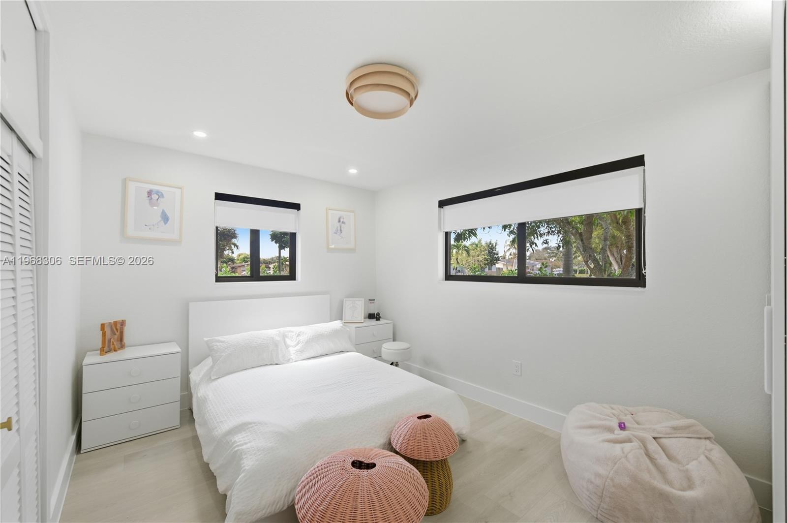 A bright bedroom features a white bed, two windows, light wood flooring, and pink ottomans — 7491 Raleigh St, Hollywood FL 33024, HOLLYWOOD, FL