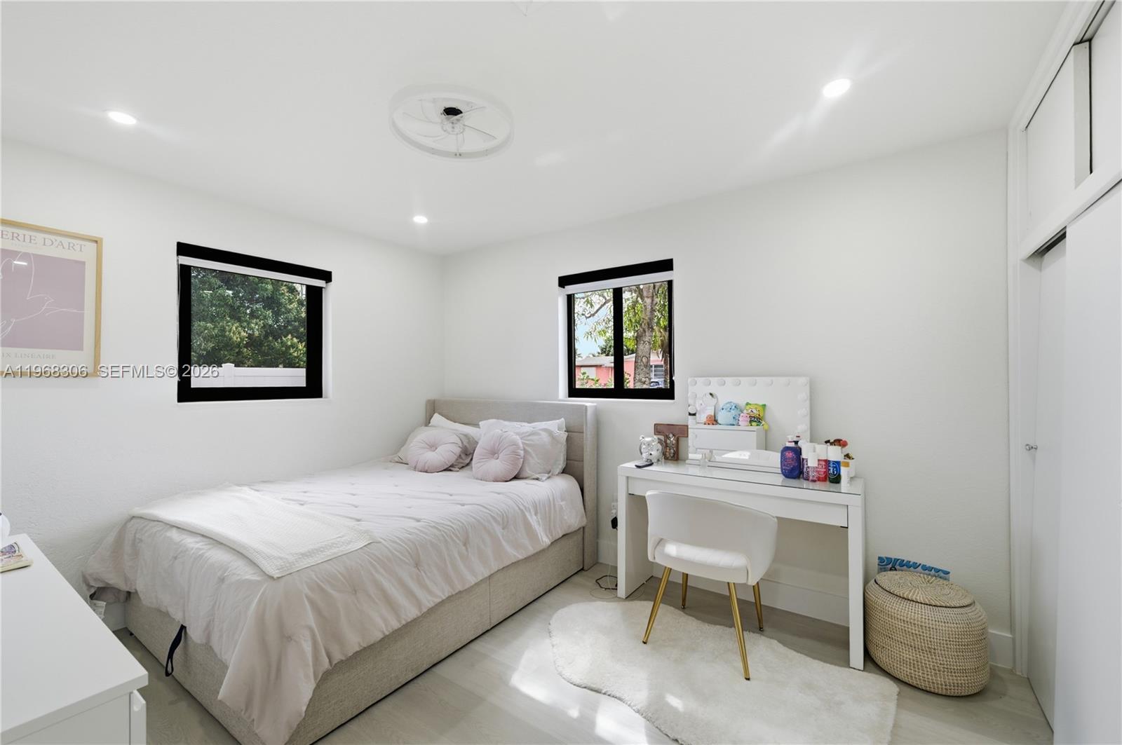 A bedroom features a bed, a vanity with a chair, and two windows with black frames — 7491 Raleigh St, Hollywood FL 33024, HOLLYWOOD, FL
