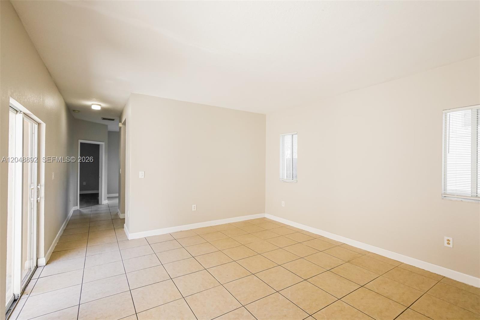 An empty room features beige walls, light-colored tile flooring, a sliding glass door, and two windows — 216 SE 32nd Ter, Homestead FL 33033, HOMESTEAD, FL
