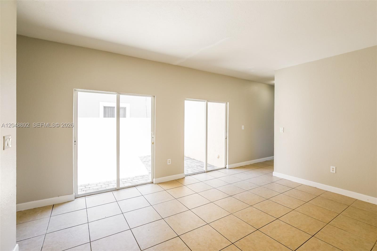 An empty room features beige tiled floors, light-colored walls, and two sliding glass doors — 216 SE 32nd Ter, Homestead FL 33033, HOMESTEAD, FL