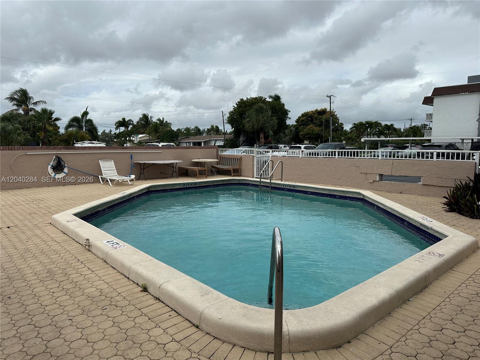 An outdoor swimming pool with a paved deck and a white fence under a cloudy sky — 1100 SE 4th Ave # 32, Deerfield Beach FL 33441, DEERFIELD BEACH, FL