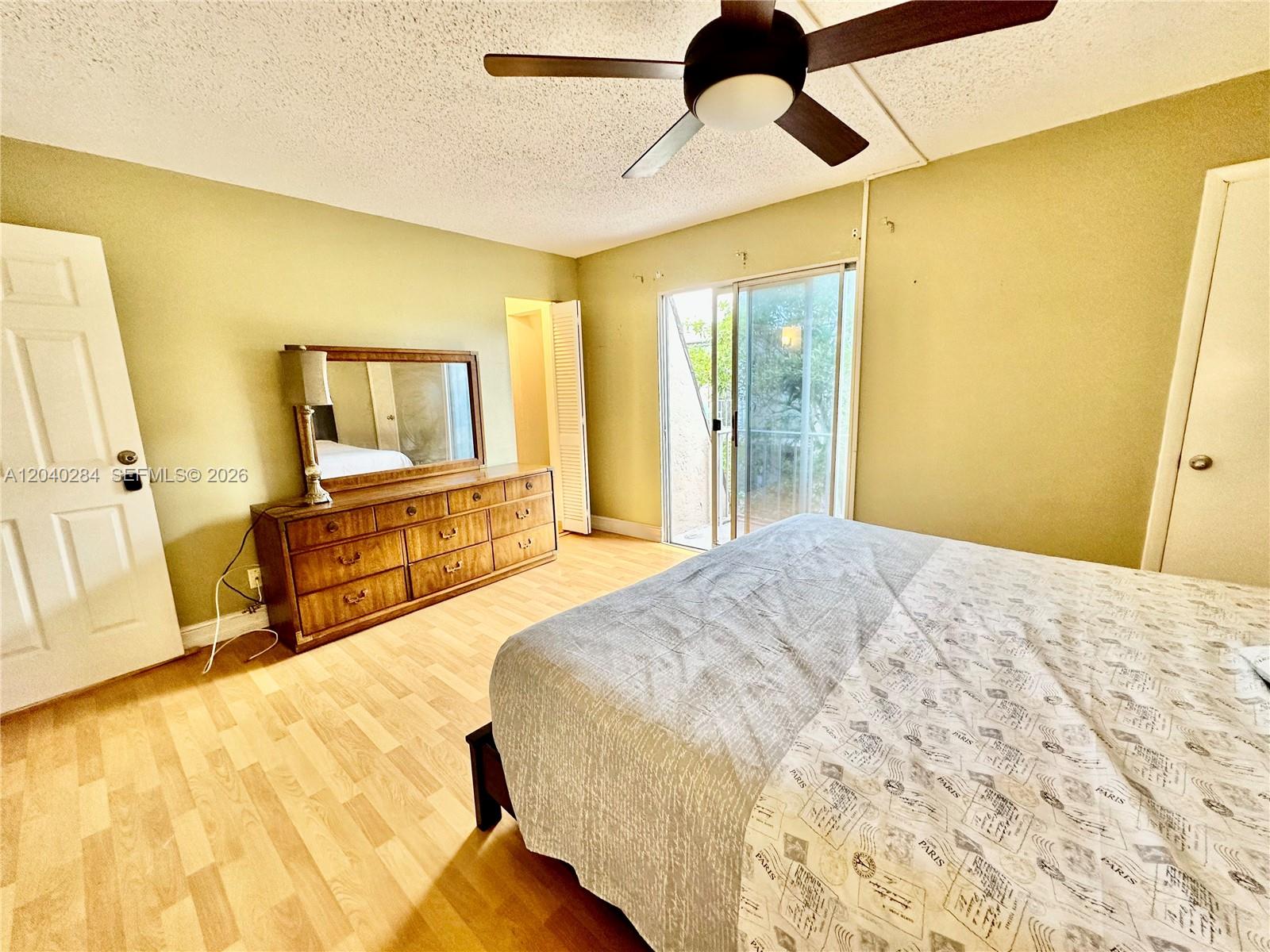 A bedroom features light wood flooring, a wooden dresser with a mirror, and sliding glass doors — 1100 SE 4th Ave # 32, Deerfield Beach FL 33441, DEERFIELD BEACH, FL
