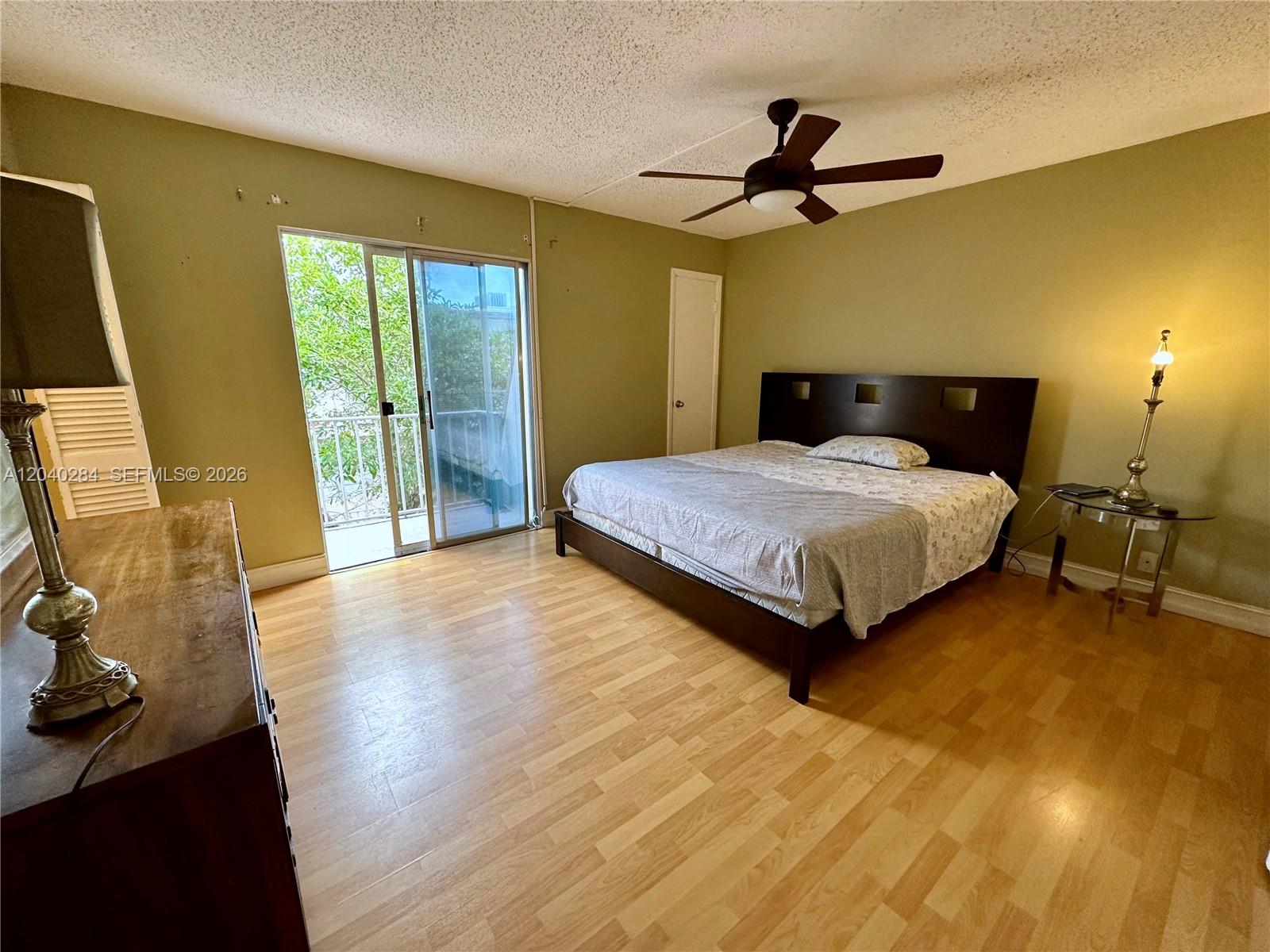 A bedroom features light wood flooring, a dark bed frame, and a sliding glass door — 1100 SE 4th Ave # 32, Deerfield Beach FL 33441, DEERFIELD BEACH, FL