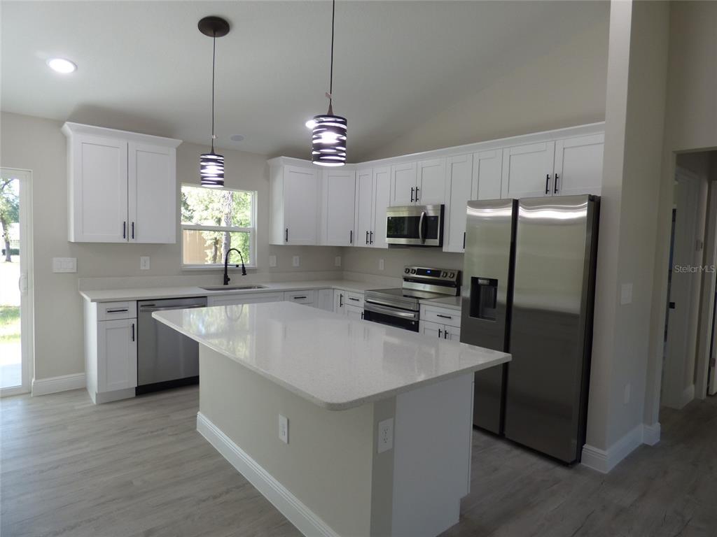 A modern kitchen features white cabinets, stainless steel appliances, a quartz island, and pendant lighting — 8114 N VOYAGER DRIVE, CITRUS SPRINGS, FL