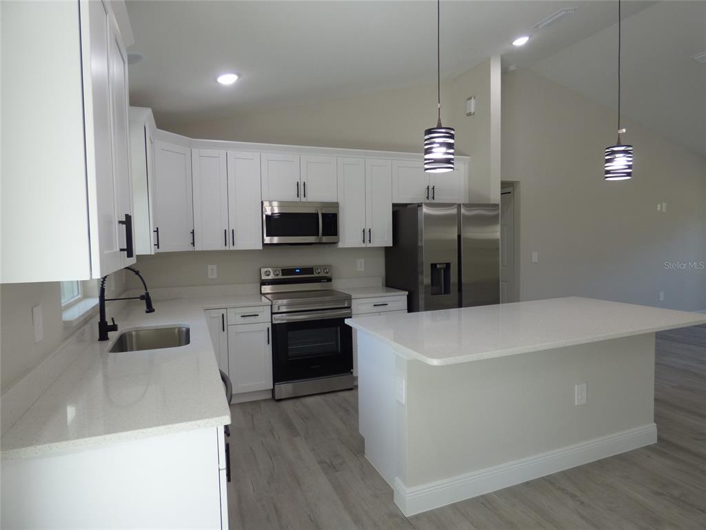 A modern kitchen features white cabinets, stainless steel appliances, quartz countertops, and a central island — 8114 N VOYAGER DRIVE, CITRUS SPRINGS, FL
