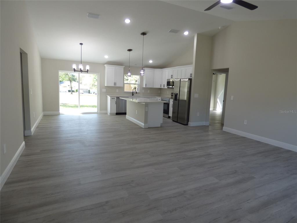 An open-concept kitchen and living area features white cabinetry, stainless steel appliances, and gray flooring — 8114 N VOYAGER DRIVE, CITRUS SPRINGS, FL