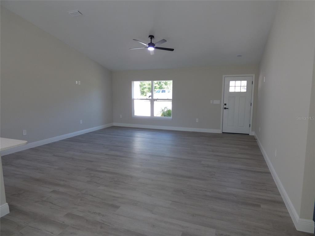 An open living room features light gray wood-look flooring, a ceiling fan, and a door — 8114 N VOYAGER DRIVE, CITRUS SPRINGS, FL