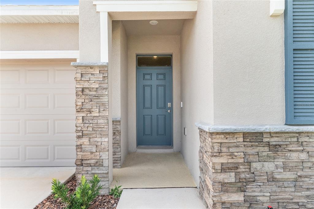 A blue front door is recessed between stone-accented walls next to a garage — 9358 SW 60TH TERRACE ROAD, OCALA, FL
