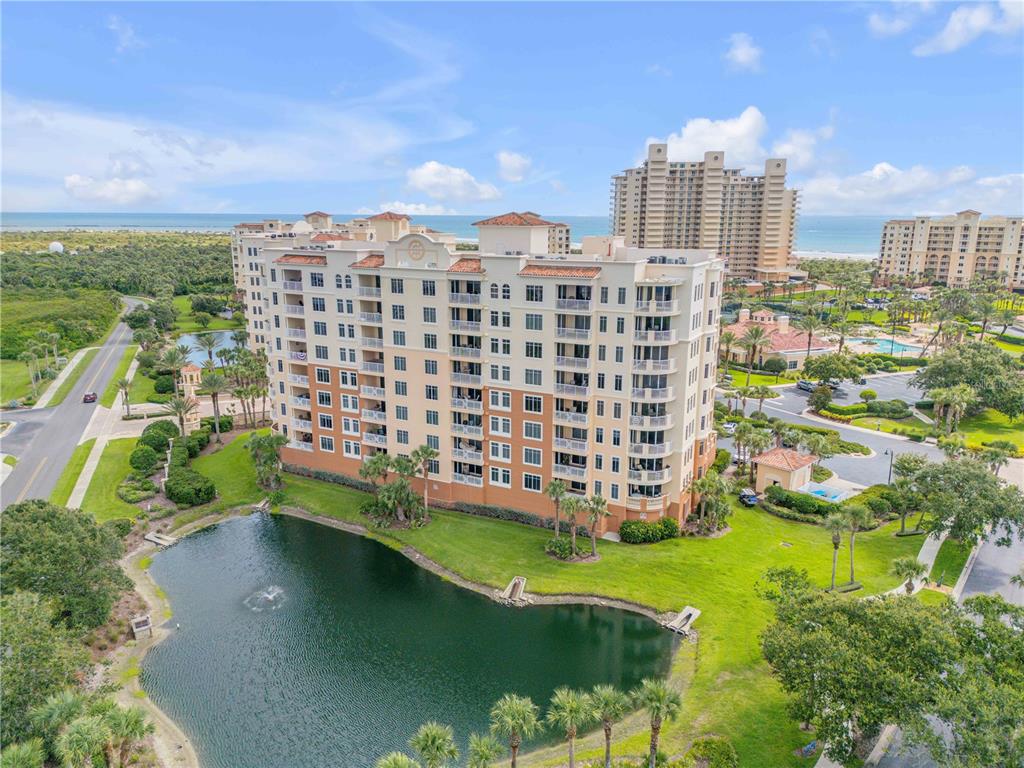 An aerial view shows a multi-story residential building situated next to a pond and road — 265 MINORCA BEACH WAY UNIT 404, NEW SMYRNA BEACH, FL