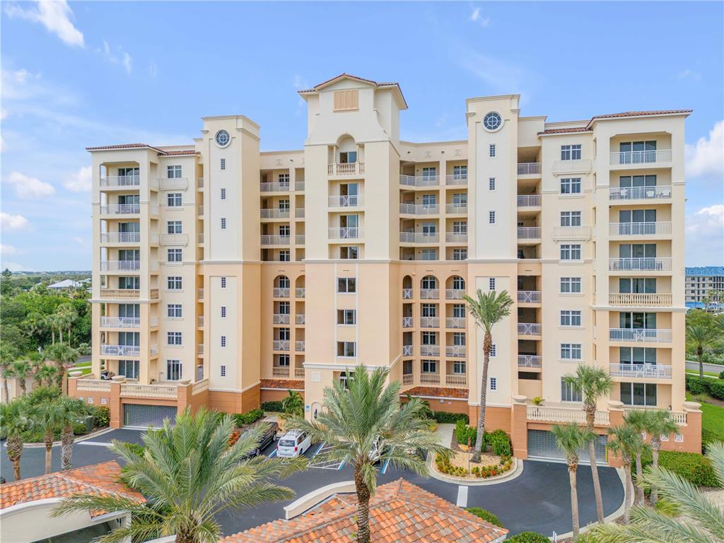 A multi-story beige apartment building with balconies and palm trees in the foreground — 265 MINORCA BEACH WAY UNIT 404, NEW SMYRNA BEACH, FL
