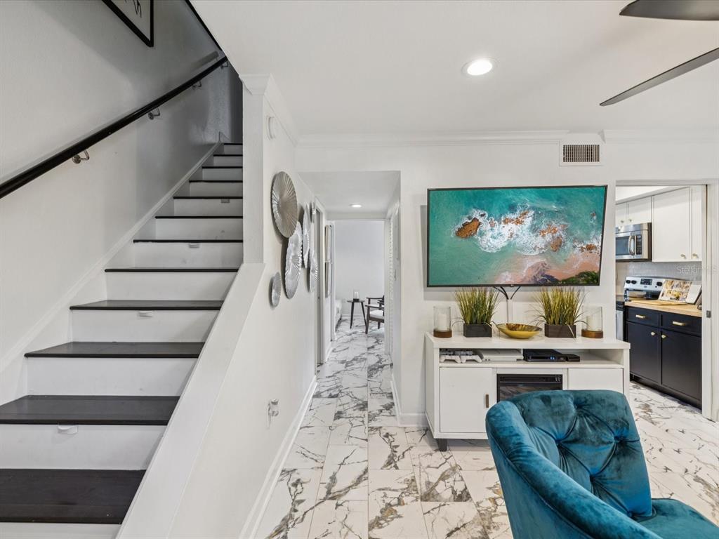 A living room features a staircase, white marble-look flooring, a wall-mounted television, and a console — 1308 70TH STREET N, ST PETERSBURG, FL