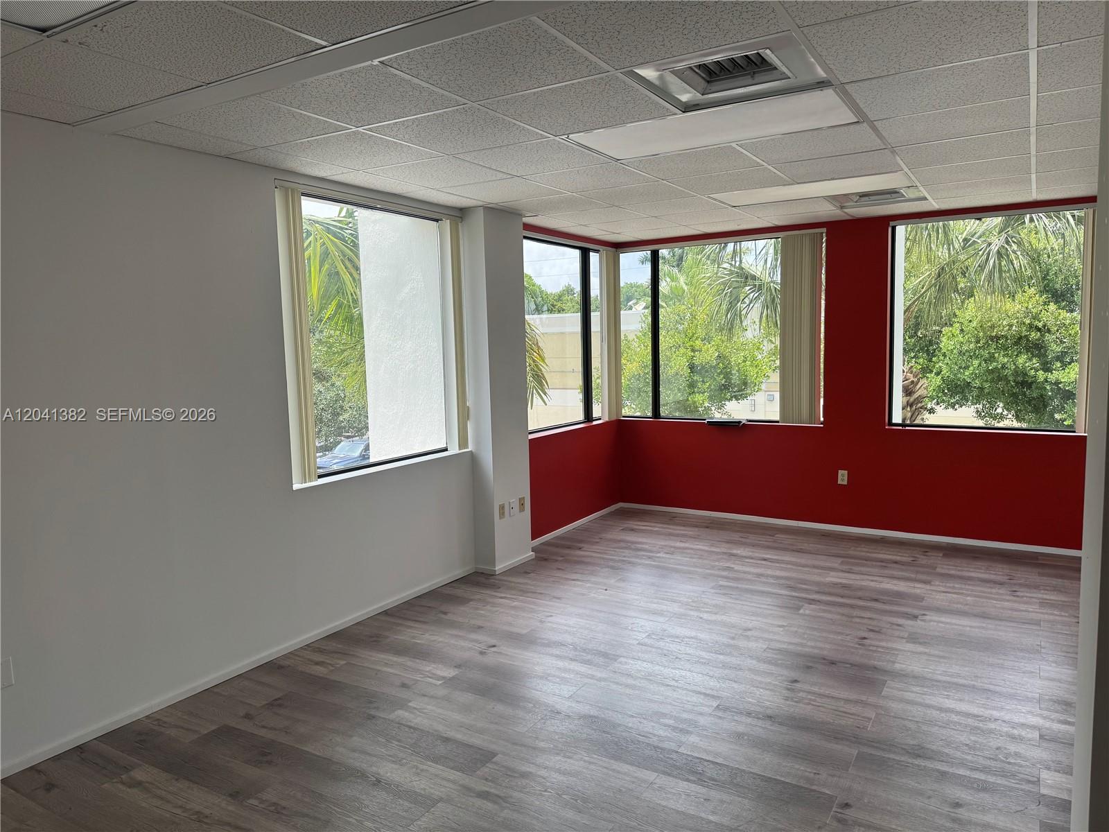 An empty office space features wood-look flooring, white walls, red accent walls, and large windows — 8700 W Flagler St # 200, Miami FL 33174, MIAMI, FL